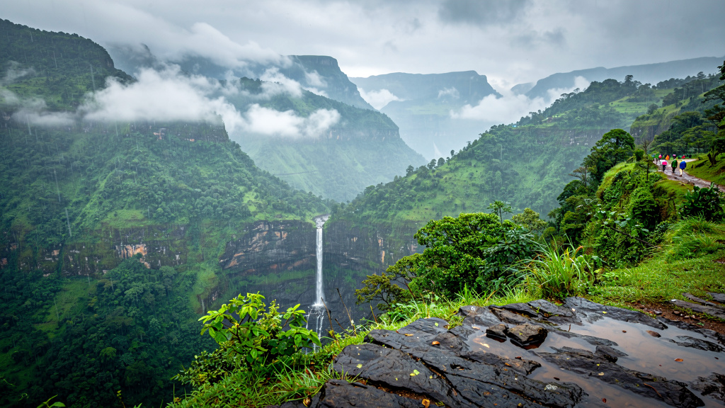 Layered mountain ridges with waterfall through misty monsoon clouds